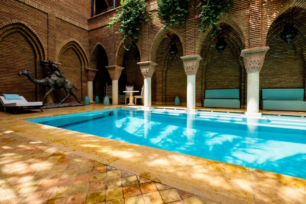 Elegant Marrakesh courtyard with a bright pool surrounded by traditional arches and greenery.